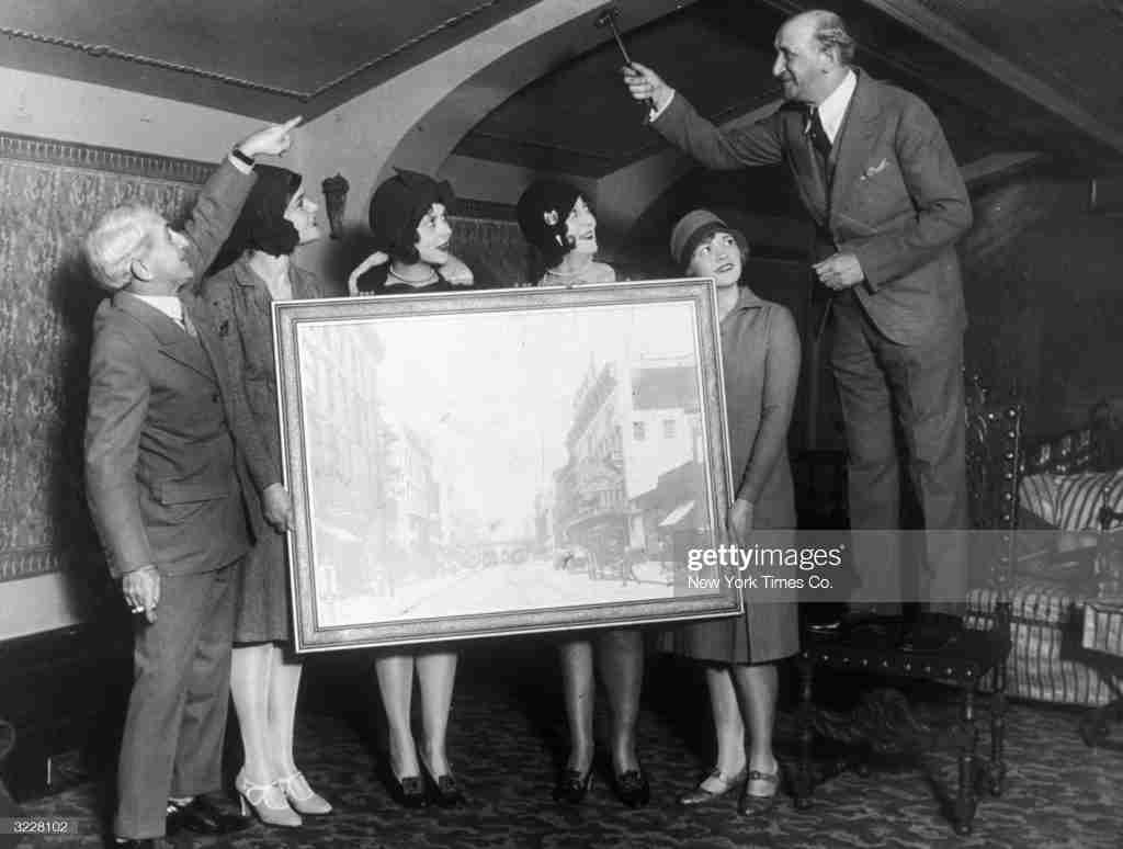 5th June 1928: Joe Weber (1867 - 1942) of the comedy duo 'Weber & Fields' presents his partner & friend Lew Fields (1867 - 1941) with a rare oil painting of the old Weber & Fields Music Hall in New York City, with the help of some 'Present Arms' show girls. (Photo by New York Times Co./Getty Images)